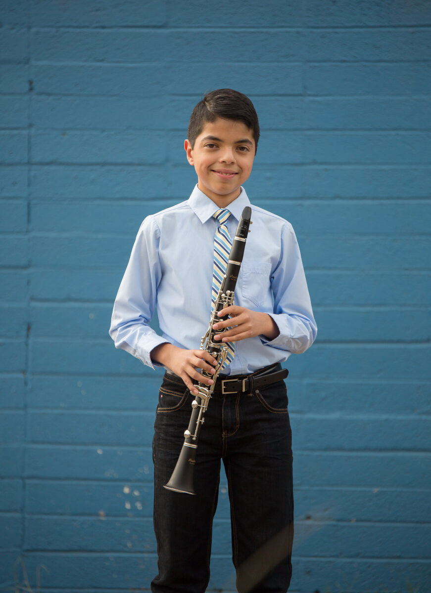 Young boy in blue shirt and black pants holds clarinet, posing for camera