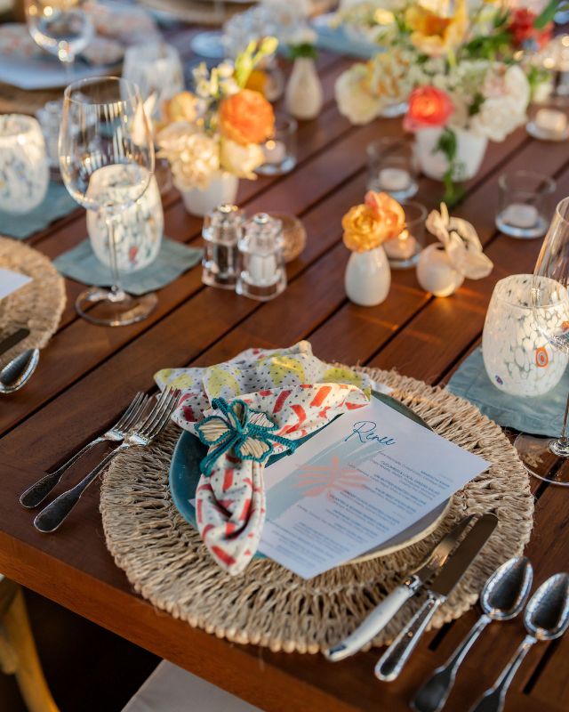 Place setting on wood table featuring a woven placemat, turquoise ceramic plate, and multicolor napkin 