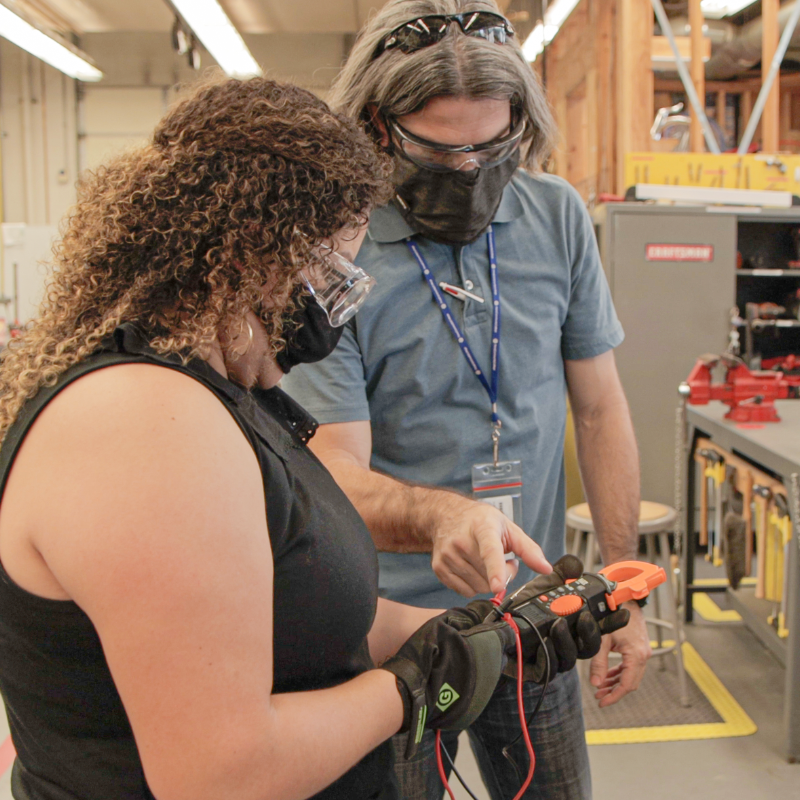 Woman and Man wearing face masks and safety goggles look at tools in a workshop