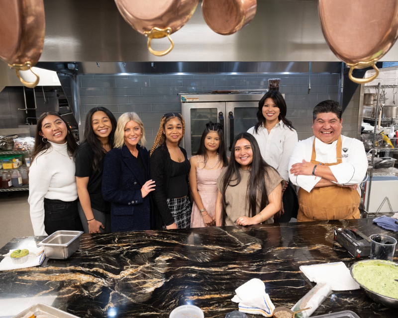 women pose in an industrial kitchen next to a male chef 