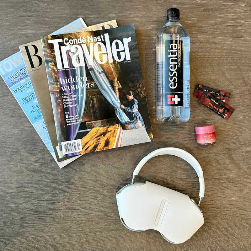 Magazines, headphones, a water bottle, electrolyte packets, and lip balm sit on a table 