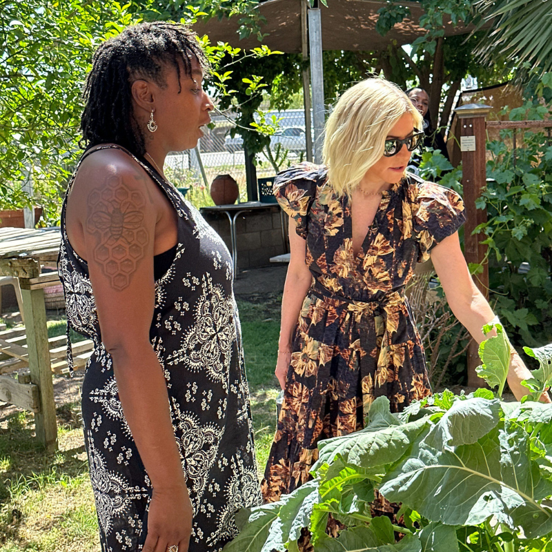 Two women look at plants growing in an outdoor garden
