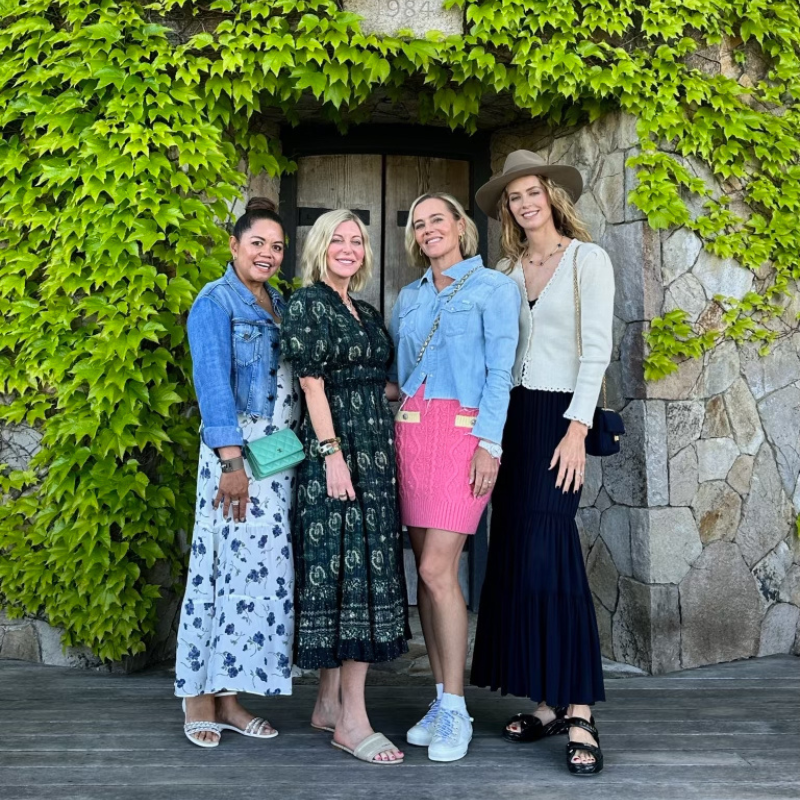 four women pose in front of an ivy covered wall
