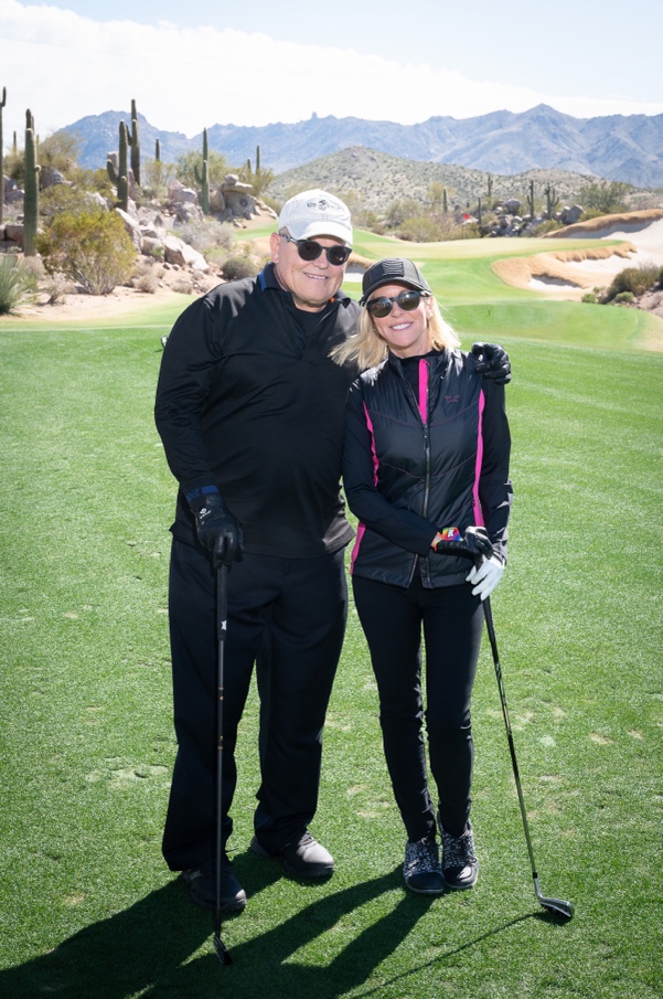 Man and woman pose in an embrace with golf clubs in their hands on a golf course