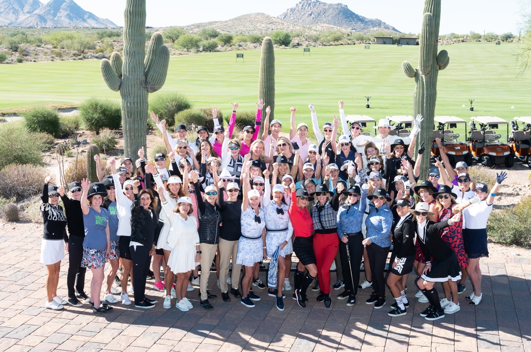 Large group of women pose with their hands up in a cheer on a golf course